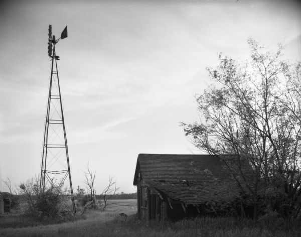 View of a dilapidated outbuilding and a windmill on an abandoned farm.