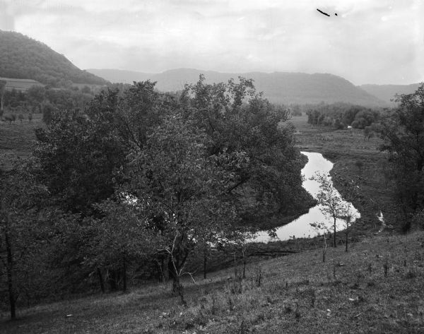 View down into small valley with stream. Bluffs are in the distance.