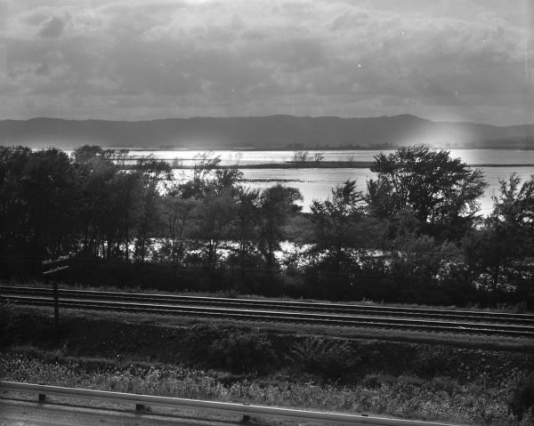 View over the CBQ railroad tracks. A tree line grows between the railroad tracks and the Mississippi River, which is visible in the background.