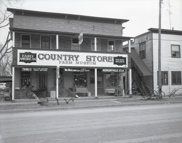 The "Early American Country Store Farm Museum." Storefront view of an antique shop with various farm implements on its front porch.