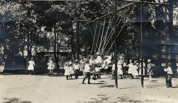 Children playing in a park playground, mainly on a large swing set.