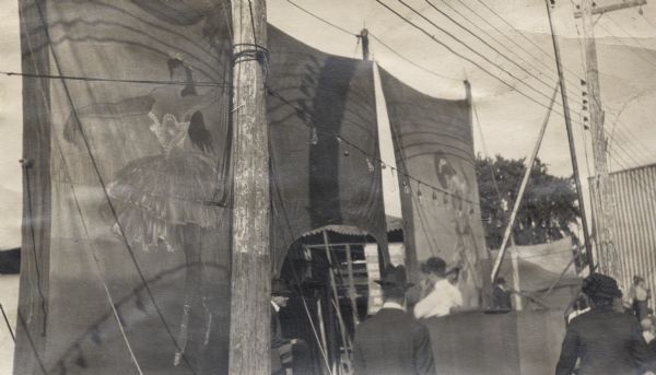 The exterior of carnival banners with people gathered in front of them. Probably depicting "Gay Paree" at the State Fair.