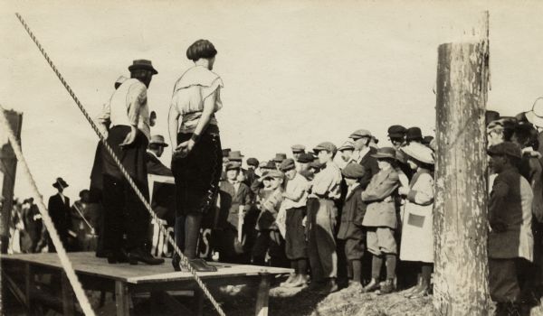 A group of several performers, possibly singers, standing outside on a platform in front of a crowd.