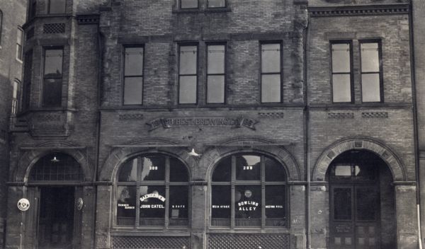 Exterior of saloon recreation center, with "1886 PH Best Brewing Co." etched onto the brick above the windows. The windows have lettering advertising "Summer Garden & Cafe" and "Bowling Alley."