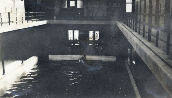 Men's day at an indoor pool. A view from the balcony on the second floor overlooking one man sitting on the edge of the pool below.