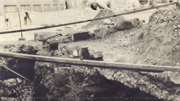 Buffalo Street construction, showing heating pipes being installed under the cut pavement. A boy is bent over in near a pile of dirt in the background looking at the work.