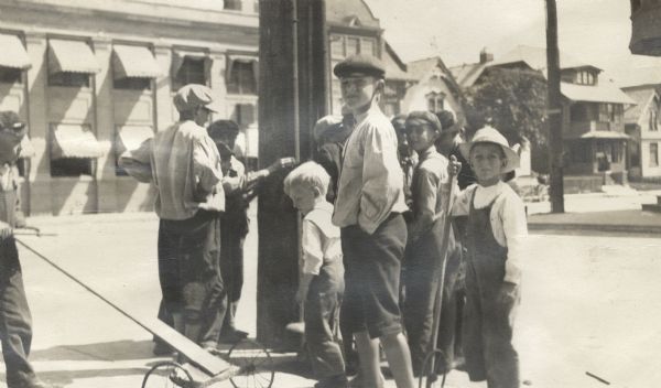A group of boys gathered around a telephone pole on a street corner, captioned: "Inquisitiveness: Getting an Electric Shock." A boy on the left has some kind of push-cart on wheels.
