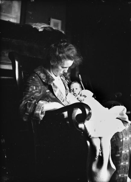 Woman in bathrobe sits in a rocking chair holding an infant.