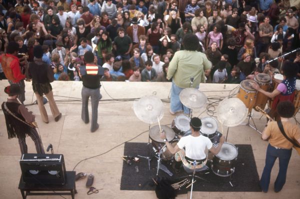 View from above of Chicago R&B act Baby Huey mid-performance. The band was made up of a three man horn section, electric guitar, drums, congas, electric bass, and the singer James Ramey, better known as "Baby Huey." There is a large crowd in front of the stage.