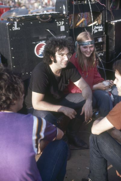 Grateful Dead guitarist Jerry Garcia with Bill Kreutzmann and Bob Weir, drummer and guitarist (respectively), sit with an unidentified woman on the Sound Storm stage before their performance.