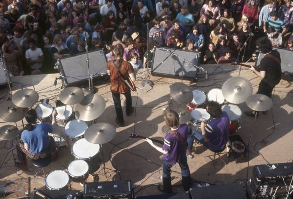 View from above of Grateful Dead on stage, featuring from left to right, Mickey Hart, Bob Weir, Phil Lesh, Bill Kreutzmann, and Jerry Garcia performing at the Sound Storm Festival. A large crowd is in front of the stage.
