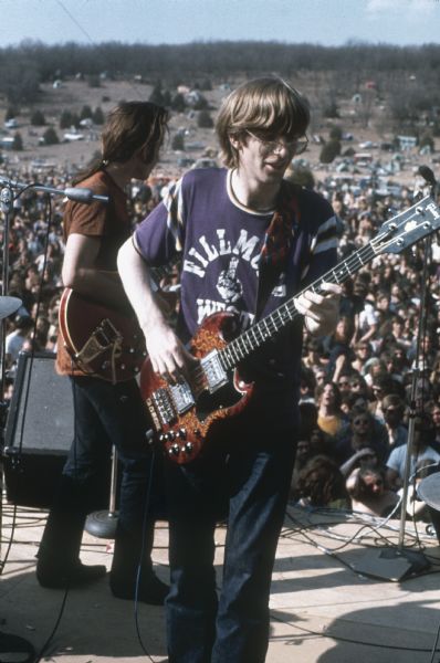 Phil Lesh and Bob Weir, bassist and guitarist (respectively) in the Grateful Dead, mid-performance at the Sound Storm festival. The bass guitar is made by Gibson, and Phil Lesh's t-shirt reads "Fillmore West." In the background is a large crowd at the York farm.