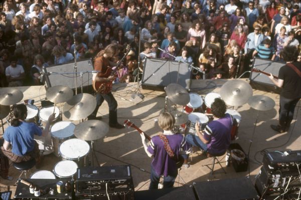 View from above of Grateful Dead, featuring from left to right, Mickey Hart, Bob Weir, Phil Lesh, Bill Kreutzmann, and Jerry Garcia performing at the Sound Storm Festival. A large crowd is in front of the stage.