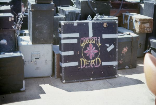 Musical equipment cases for the Grateful Dead, sitting backstage. A large case in the center is decorated with a hand-painted logo.