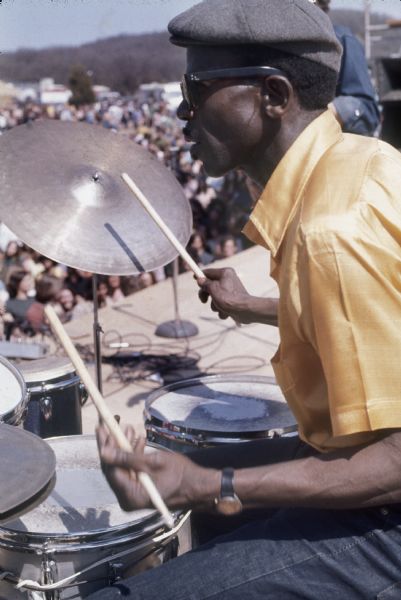 Close-up of possibly Bob Richey or Bobby Davis, on stage playing drums for Luther Allison. The audience can be seen in the background.