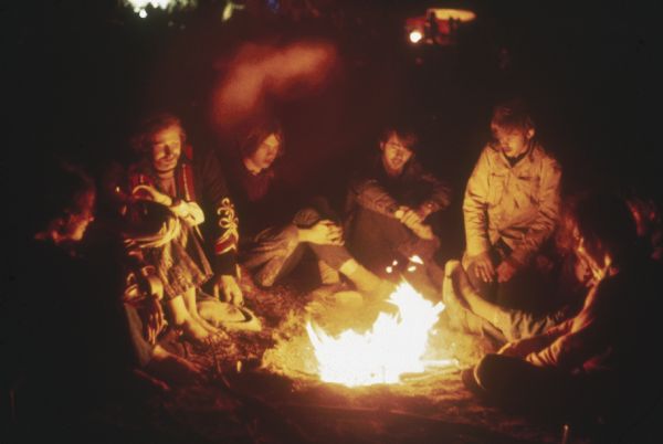 A group of young audience members crowd around a campfire in the camping area of the Sound Storm music festival.