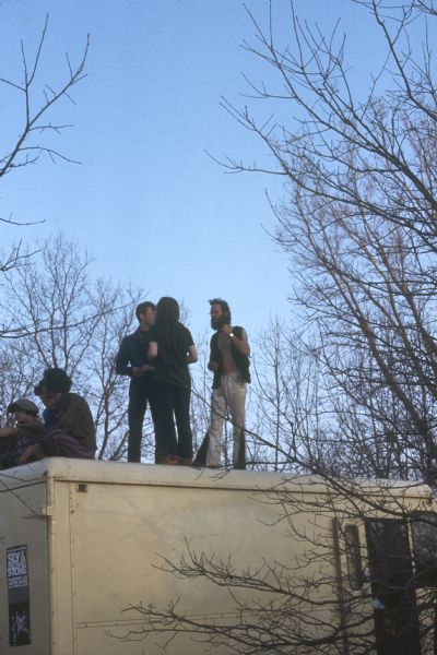 A small group of audience members crowd on top of the roof of a truck in this picture belonged to Captain Bill's Whiz Bang and the individual facing left is the organist Larry Robertson at the Sound Storm music festival.