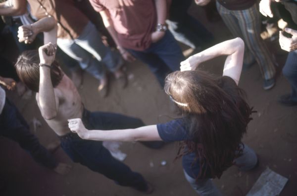 Overhead view of two people dancing in the crowded audience during the Sound Storm music festival. One of them is shirtless and the other wears a dark blue t-shirt with a headband in his or her hair.