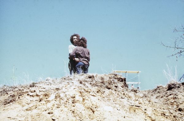 A couple take a break from the crowded audience to embrace on the edge of a steep ditch with part of the Sound Storm festival scaffolding visible behind them.