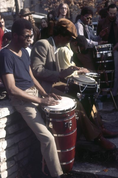 A crowd of four African American men play conga drums at the Sound Storm music festival for a gathering audience.