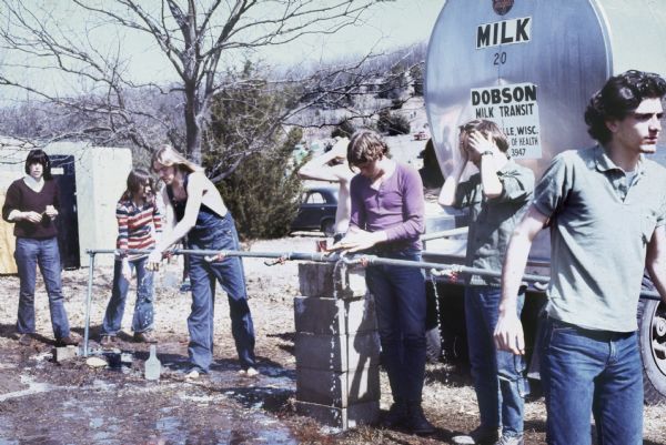 A group using water faucets connected to a milk tanker associated with "Dobson Milk Transit" while the festival stage and other amenities are still under construction.