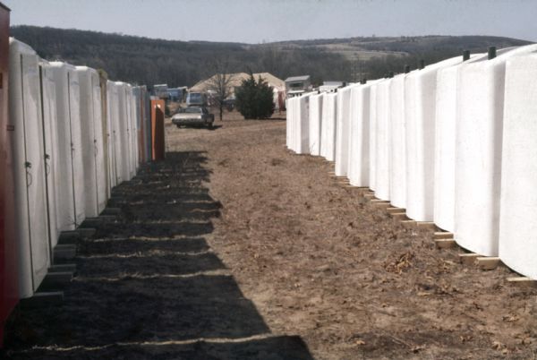 Two rows of portable toilets with automobiles and campers in the background during the construction of the festival stage.