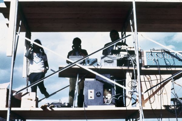 Three men positioned on the Sound Storm festival stage scaffolding maintain the electronic sound system equipment during stage construction.