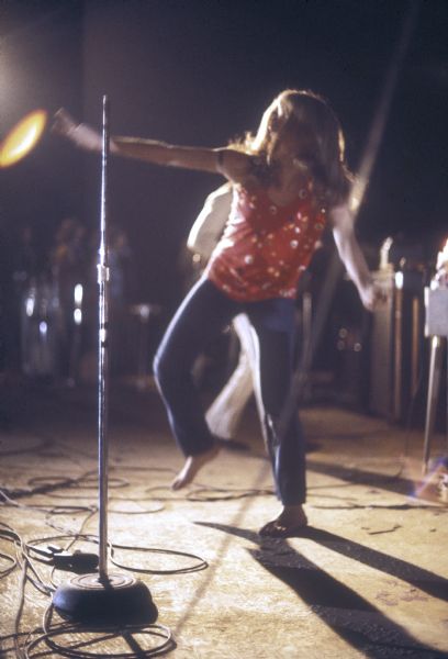 Lead singer Barbara Swenson of Northern Comfort dancing on stage with a microphone stand in the foreground. A guitarist is in the background.