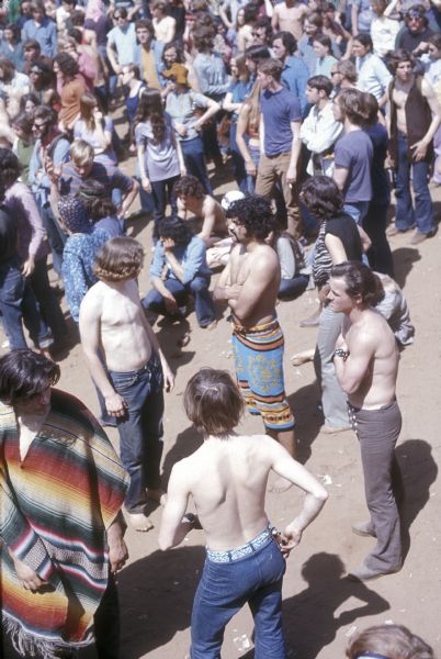 Elevated view of crowd of audience members at the Sound Storm music festival. A few of the men in the foreground are shirtless, while others are wearing either ponchos and towels.