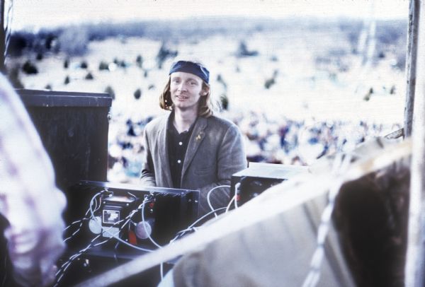 Geoff Cook, wearing a headband and a jacket, stands on the Sound Storm stage near stacks of speakers with another festival staff member. He was the festival sound engineer.