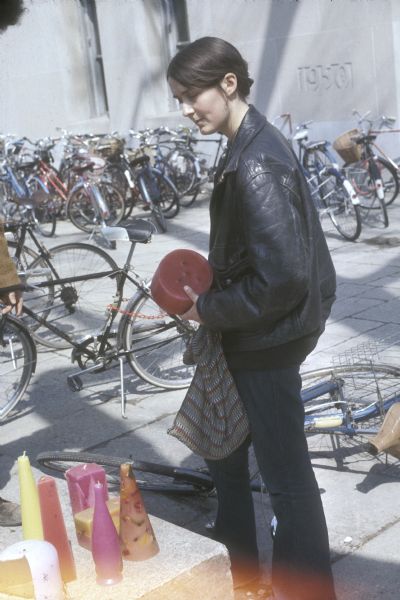 Unidentified young woman holding a large candle near a display of candles next to the University of Wisconsin-Madison Memorial Library. Bikes are parked in the background.