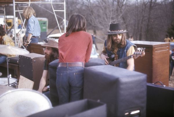 Members of country rock band Mason Proffit, Rick Durett (keyboards), Art Nash (drums), and John Talbot (bass) hang out backstage at the Sound Storm music festival before performing. While Tim Ayres was the usual bass player for the group, Talbot appears to have taken bass guitar duty for this performance.