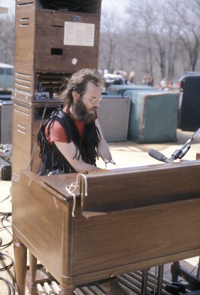 Larry Robertson, keyboardist for Captain Billy's Whiz Band wearing a fringed vest performing on stage at the Sound Storm music festival. There is a stack of rotating "leslie" speakers behind him.