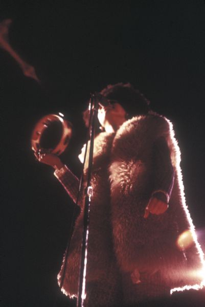 View from below stage of singer Minnie Riperton performing with psychedelic soul band Rotary Connection at the Sound Storm music festival. She is wearing a long furry vest and is playing a tambourine.