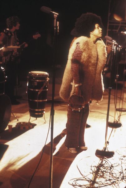 Singer Minnie Riperton, wearing a long, furry vest and holding a tambourine, performing with psychedelic soul band Rotary Connection on stage at the Sound Storm music festival.