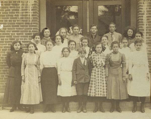 Contest winners pose outside brick building in doorway. The children are wearing ribbons on their lapels or collars. 
First row, reading from left to right: Florence Barr, Katharina Rauch, Mary Schauf, Josephine Berntgen, Willie Wieland, Bessie Di Vall, Nellie Drinkwater, Gladys Ruchti 
Second row: Olga Doeringfeld, Olive M. Bremmer, Susie Walz, Florence Vesperman, Francis Grimm, Ester Kreul, Norma Doeringfeld
Third row: Daisy Edge, Lela Beetham, Jeane Roberts, Adam Jamison, Ralph Orton, Erma Gulick