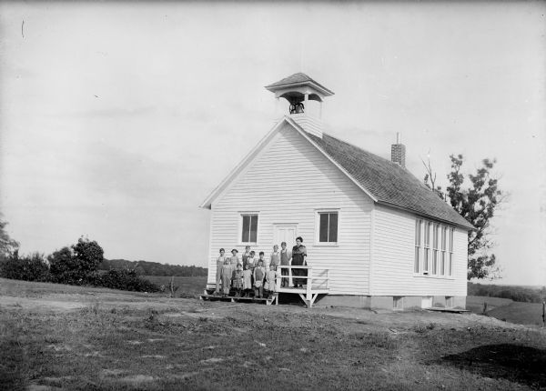 Little Grant teacher and students stand on the front steps of a new clapboard school building with bell tower. Erected in 1913.