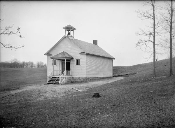 One-room schoolhouse of clapboard with a front door gable roof and a bell tower.