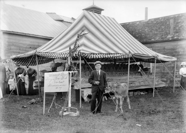 Jeffie Duncan, winner of first prize in corn contest, and calf, Lawn Mower, stand before tent exhibiting the Boys Corn Club Contest.