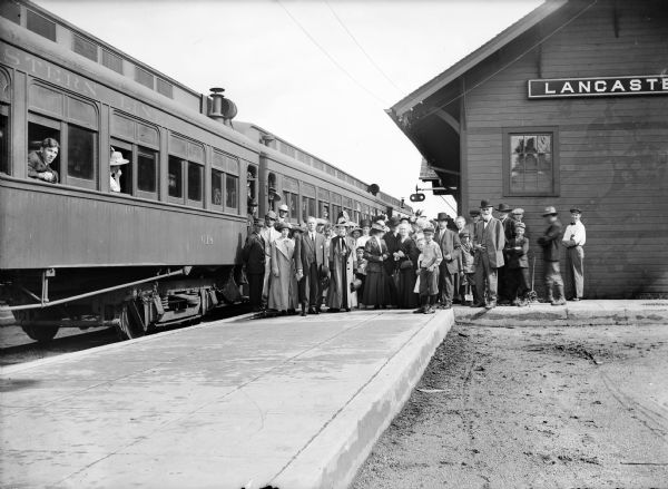 Group of people posing on platform at train station next to train.