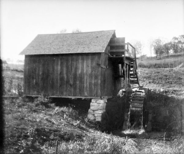 Small wooden building with water wheel, presumably a mill.