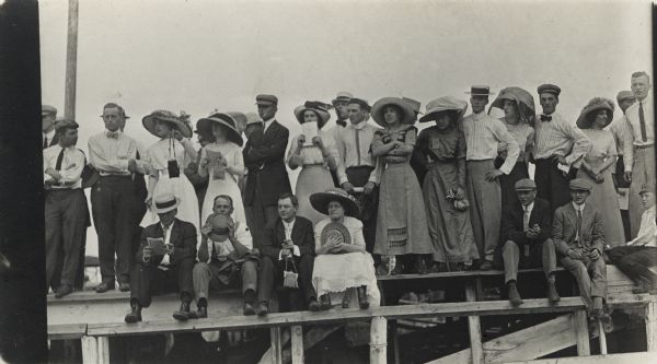 Crowd of men and women on grandstand bleachers watching a sporting event.