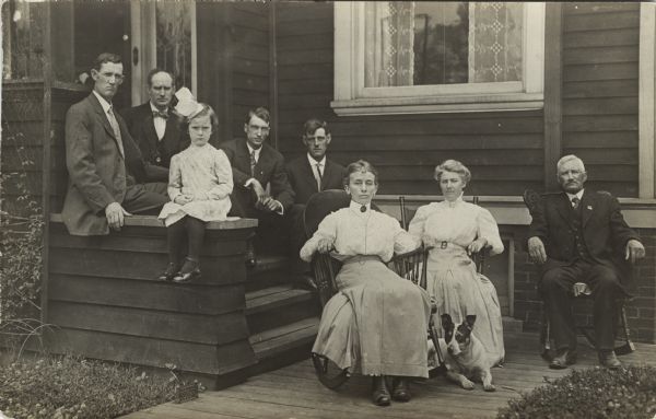 Group portrait of a family with a dog sitting on and around the front porch of a house.