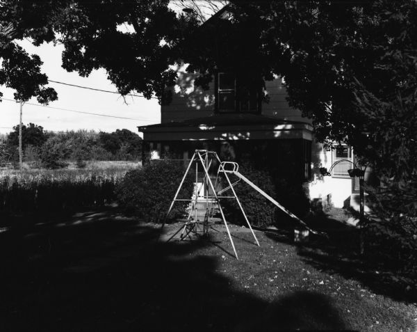 Backyard of a house with a swing set and slide shaded by trees.