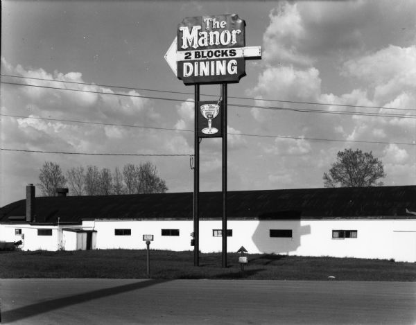 An electric sign for "The Manor / 2 Blocks / Dining" towers over a long, one-story building.