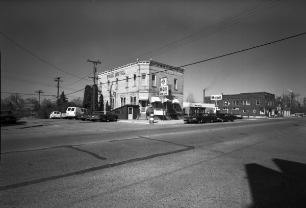 View across street of parked cars along curb in front of the Suburban Inn, formerly the Park Hotel, on the 300 block of Broom Street. Next door on the right is a Mobil service station.