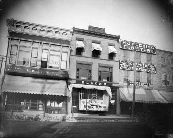 Looking east across Pine street at the storefronts of J. Wien's clothing, dry goods, and grocery store, Black's Dry Goods store, Schwaller's Real Estate Office, and H.J. Roesing Furniture store.  Jacob Wien moved his business to the former Riel store space in August 1904.
