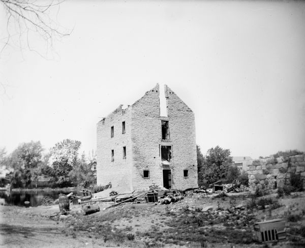 Exterior view of a burned-out stone building with a missing roof next to a pond.