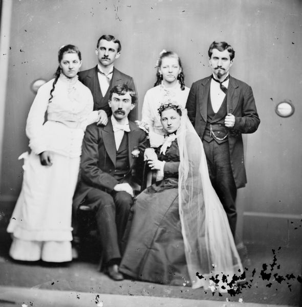 A group of three women and three men gather to pose for an indoor wedding portrait.