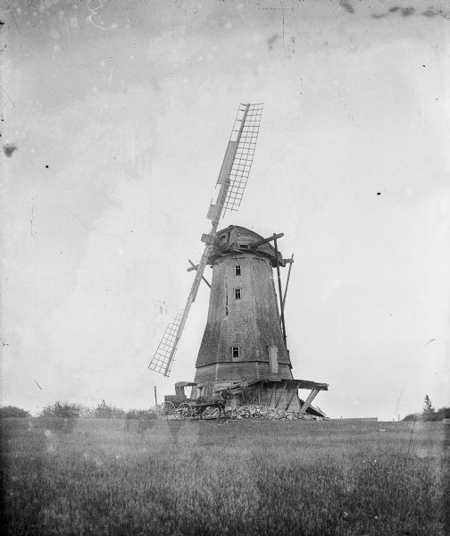 A large windmill in a rural setting. A man and horse-drawn vehicle are parked in front of the windmill.